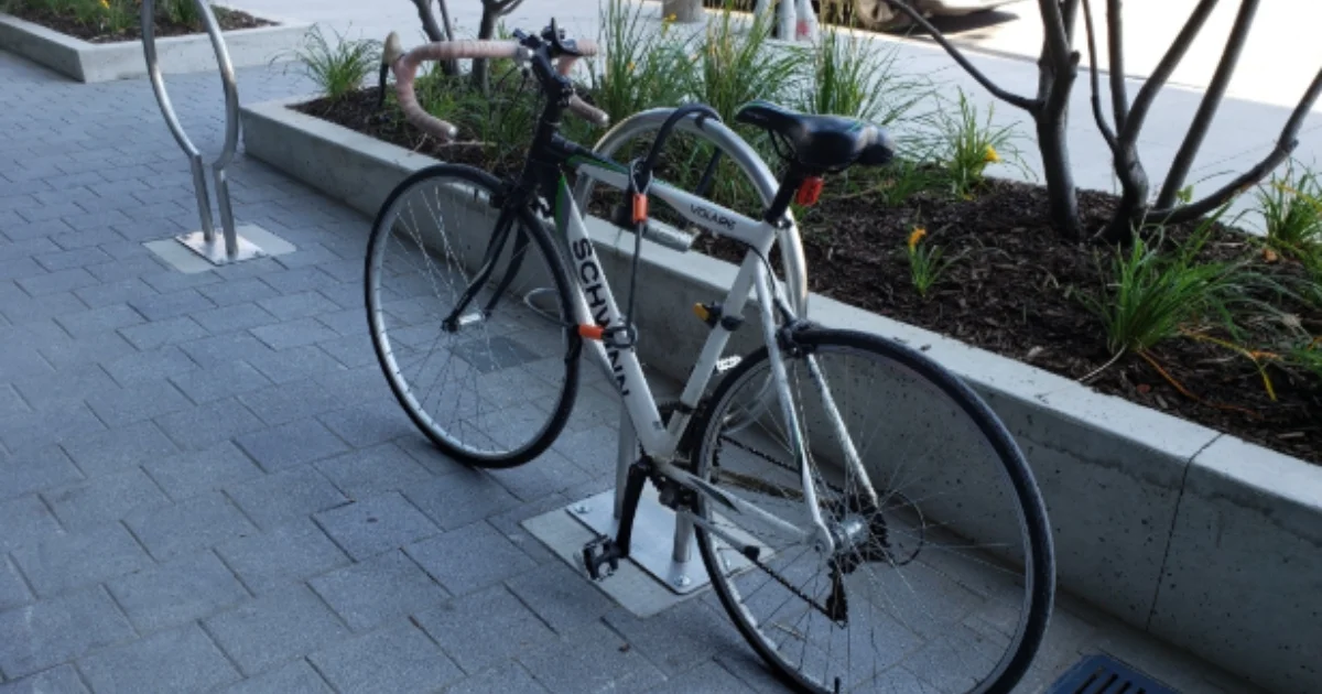 A white and black Schwinn bicycle locked to a silver bike rack on a modern sidewalk.